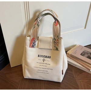 Detail of canvas bucket bag with floral texture handles and printed text on wood floor