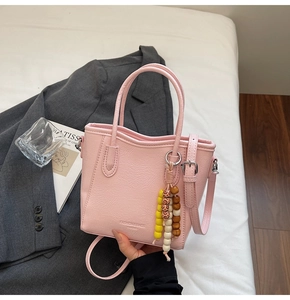 Detail of pink lychee leather tote bag featuring a beaded charm and adjustable strap