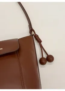 Detail of dark brown leather shoulder bag featuring spherical charm and gold hardware