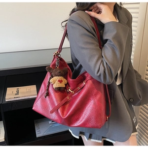 Close-up of red pebbled leather tote bag with a cute brown bear charm on gray blazer