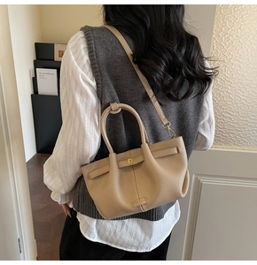 Beige pebble leather tote bag with crossbody strap shown on model in a cozy indoor setting