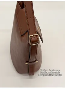 Detail of brown leather bucket bag featuring adjustable strap and custom metal buckle hardware