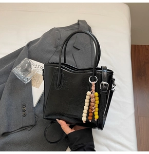 Detail of a shiny black bucket bag with dual handles and a colorful beaded pendant