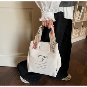 Detail of canvas tote bag featuring floral embroidered handle and minimalist printed text