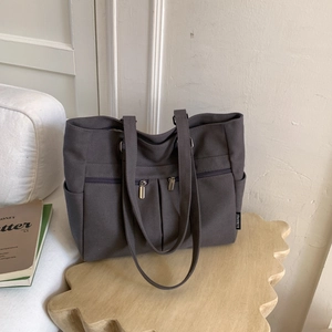 Detail view of a large dark grey canvas tote bag with functional pockets on a wooden tray