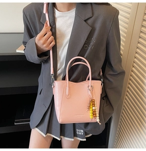 Detailed shot of a pink crossbody bucket bag featuring a colorful beaded charm and metal strap