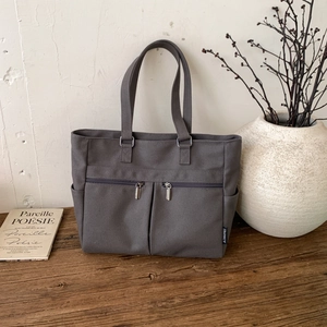 Detail of grey canvas tote bag featuring dual front zipper pockets and side pockets