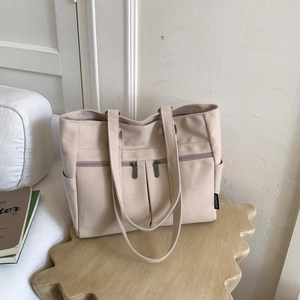 Close-up of cream canvas tote bag with multi-pocket design and wide shoulder straps