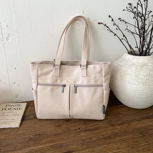 Detail of off-white canvas tote bag with dual front zippers on rustic wood tabletop
