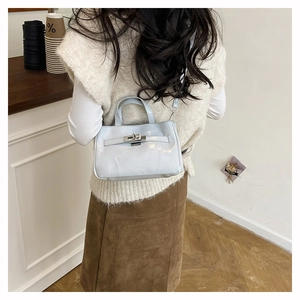 Détail du sac seau bleu clair avec boucle métallique et bandoulière dans un café