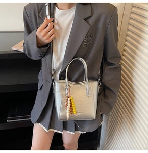 Detail of silver metallic bucket bag with beaded charm and adjustable strap on a model