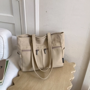 Detail of beige canvas tote bag with front dual zipper pockets and side pockets