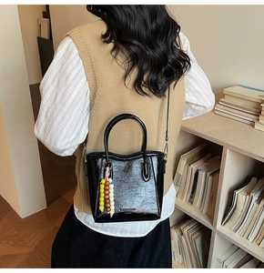 Detail of black glossy bucket bag with bead pendant shown on model in library