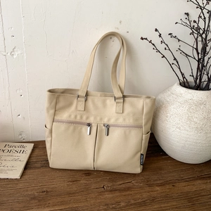 Detail of beige canvas tote bag with dual front zippers on a rustic wooden desk