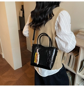 Detail of black glossy bucket bag with colorful beaded charm and slim shoulder strap