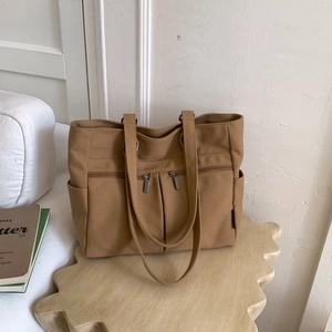 Close-up of khaki canvas tote bag with front zipper pockets on wooden display stand