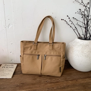 Detailed view of khaki canvas tote bag with functional pockets on a rustic wooden desk