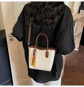 Detail of cream white leather bucket bag featuring dark brown handles and colorful bead charm