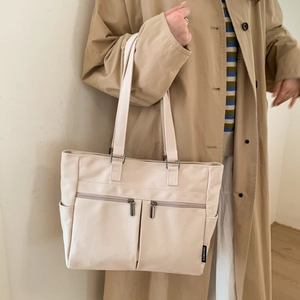 Detail view of large cream canvas tote bag showing front zip pockets and side pockets