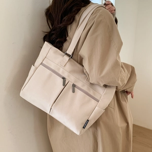 Detail of canvas tote bag showing front zipper pockets and side pouch in beige