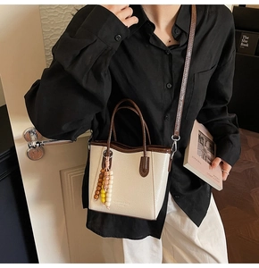 Close-up of cream PU leather handbag with beaded charm and plaid strap detail