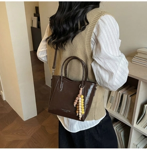 Detail showing high-gloss brown leather bucket bag with decorative beads and printed text