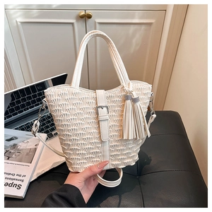 Detailed close-up of cream pleated bucket bag with tassel charm and thin strap