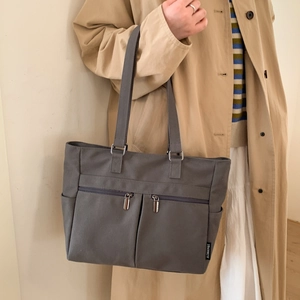 Detailed view of dark grey canvas tote bag with metal zippers and side pocket texture