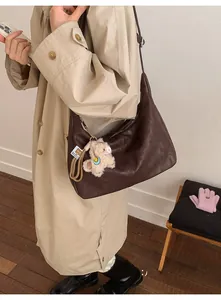 Detail of dark brown leather crescent bag featuring a cute cream lamb charm and adjustable strap