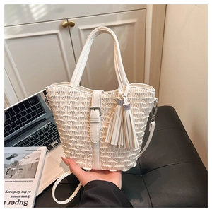 Detail shot of white pleated bucket bag with tassel charms on a leather bench