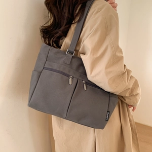 Close-up of grey canvas tote bag showing dual zippered pockets and metal hardware details
