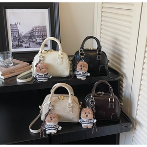 Row of Boston handbags in cream, black and tan with cute bear charms on a display stand