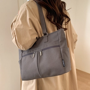 Side view of dark grey canvas tote bag with multi-pocket details worn over a trench coat