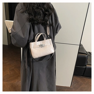 Détail d'un sac seau luxe beige avec fermoir argenté et poignée porté sur un trench-coat