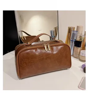 Detail showing the brown crocodile texture and gold double zipper of the travel bag