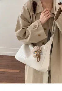White crescent tote bag with plush charm shown worn by a model in a minimal setting