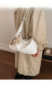 Detail of white glossy leather tote bag featuring a cute brown plush bear charm