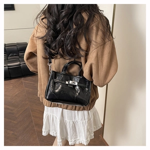 Détail du sac seau en cuir verni noir brillant avec boucle argentée et bandoulière