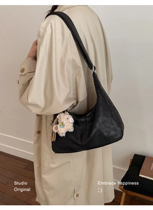 Detail of black leather crescent bag with white plush bear charm and silver buckle