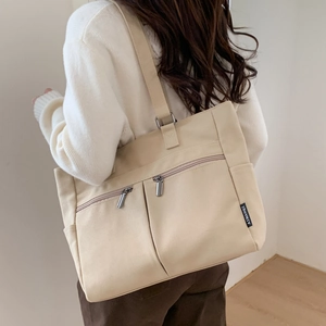Detail of beige canvas tote bag with metal zipper pockets and wide shoulder straps