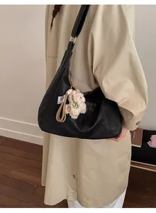 Close-up of black leather crescent bag with a cute sheep plush charm on a shoulder strap