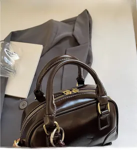 Detail of dark brown leather Boston bag with dual handles and gold-tone hardware