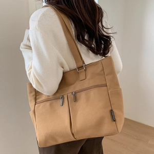 Close-up of large khaki canvas tote bag featuring double front zip pockets and side pockets