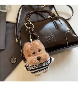 Brown plush puppy keychain in striped sweater attached to a leather handbag