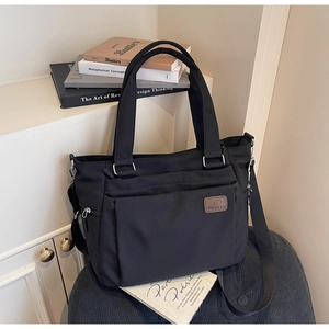 Detail of durable black nylon tote bag showing adjustable straps and brown brand label