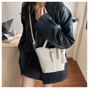Close-up of a cream woven bucket bag with elegant pleats and leather tassel detail