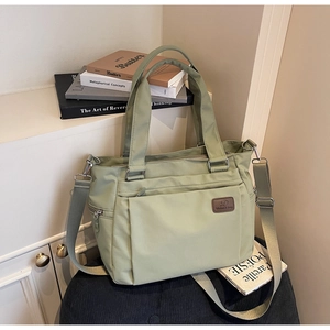 Detail of sage green nylon tote bag with brown leather logo and adjustable strap