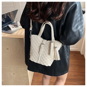 Detail of cream woven bucket bag with fringe tassels and metal buckle on leather jacket