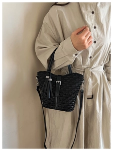 Detail of a black pleated bucket bag with tassel charm and sleek metal buckle strap