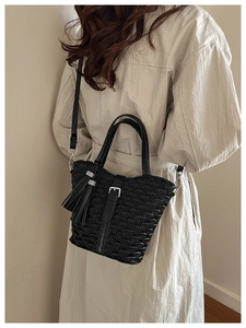 Detail of black pleated bucket bag with tassel accent and adjustable silver buckle strap